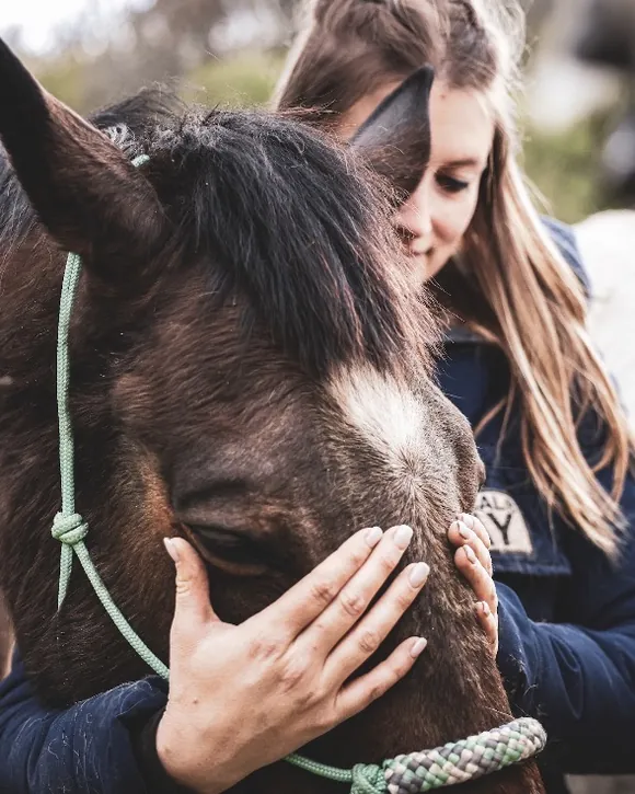 Marie Clément pose les mains sur la tête d'un cheval bai