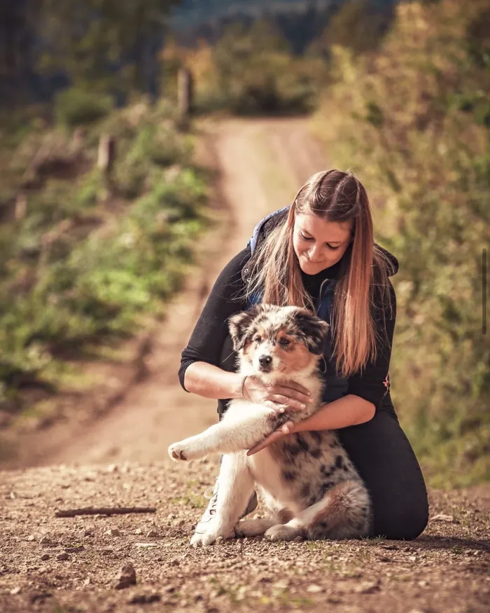 Marie Clément tient dans ses bras un chiot berger australien, sur un chemin